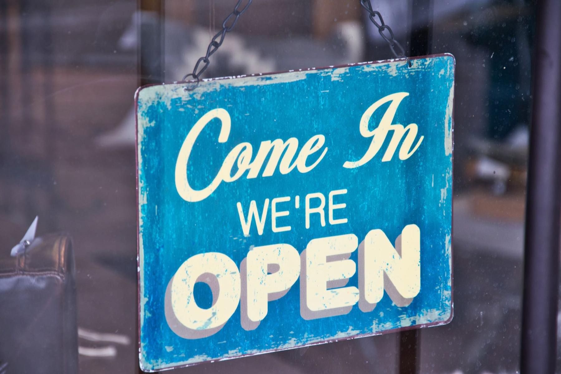 Blue Come In We're Open sign hanging inside a shop window